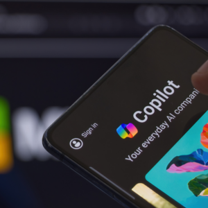 Copilot icon visible on mobile phone screen, Microsoft logo in the background.