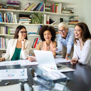 Four women engaged in discussion around a table, with a laptop open in front of them, fostering collaboration and ideas.