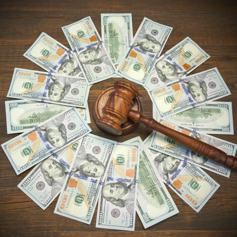 A gavel positioned on top of currency, displayed on a wooden surface, representing the intersection of law and advanced client costs for attorneys.