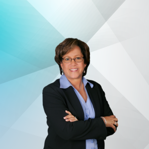 A professional woman smiling in a corporate headshot. She is wearing a black blazer, a blue collar shirt and has short brown hair.